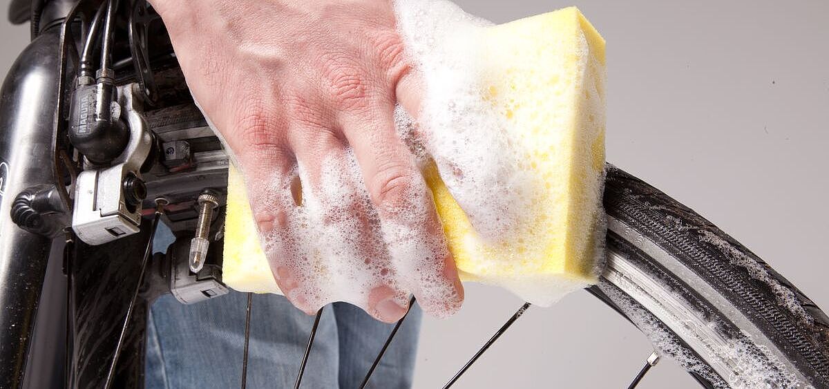 Pflege Großaufnahme einer Hand mit Schwamm und Schaum, die ein Fahrrad-Vorderrad säubert.